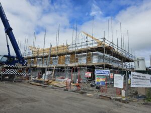 Photograph of Cwrt Y Rhos develpment. In the centre of the image are timber frame structures for the new homes. To the left of the image is a blue crane.