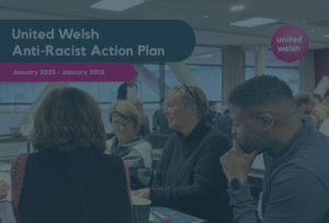 An image of the front cover of United Welsh Anti-Racist Action Plan. Cover is a photo of a man and three women at a table having a meeting with a navy filter over it. At the top left of the photo is a navy speech bubble with white text that reads 'United Welsh Anti-Racist Action Plan.' Below it is a pink speech bubble with white text that reads 'January 2025 - 2026'