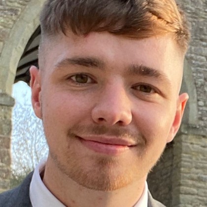 A photo of a young man with brown hair, smiling at the camera